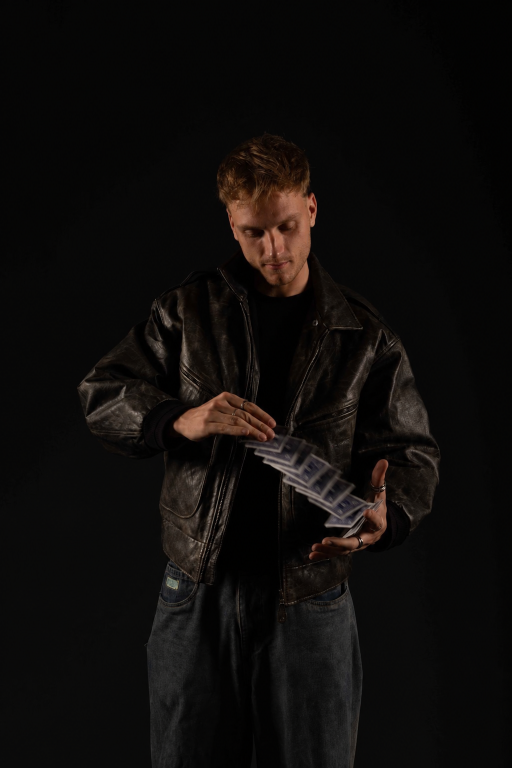 Maxi in Lederjacke blickt auf die fallenden Spielkarten zwischen seinen Händen